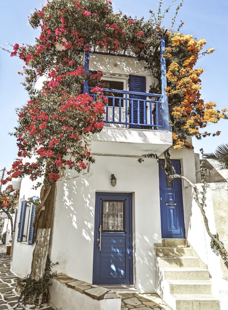 House with blue doors, a balcony and flowering plants, illustrating the cost of owning a home in Greece